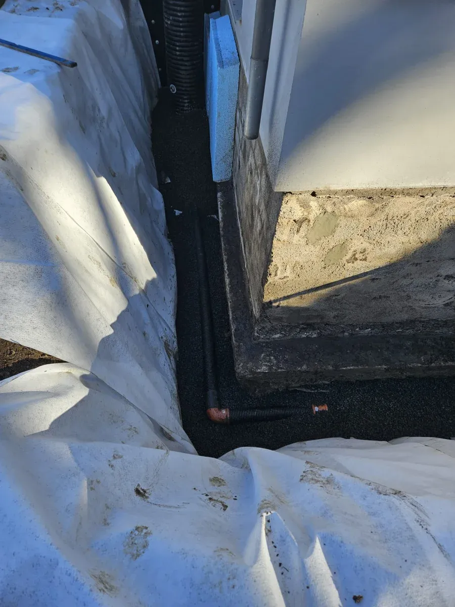 Svarta dräneringsrör med isolering och geotextil runt husgrund